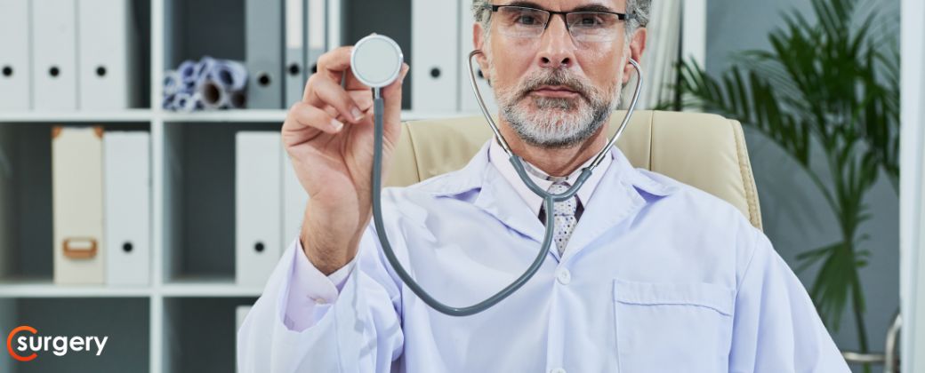 באיזה גיל מקבלים קילה? - ניתן לראות רופא עם זקן מביט למצלמה. בצד שמאל למטה לוגו אתר surgery