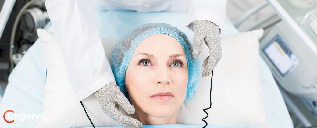 אישה עומדת להיות מורדמת לקראת ניתוח למפקטומיה, יש לה כיסוי על הראש ובצד שמאל למטה לוגו אתר surgery