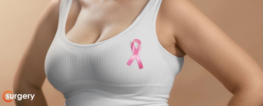 ניתן לראות פלג גוף עליון של בחורה עם גוזייה לבנה והיא עונדת תגית או מדבקה של מלחמה נגד סרטן השד. בצד שמאל למטה לוגו אתר surgery